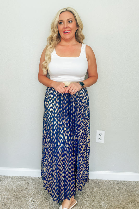 Blonde woman smiling in a white scoop neck tank top and the Monaco Metallic Pleated Skirt, a blue and gold chevron maxi skirt from an online Southern boutique.