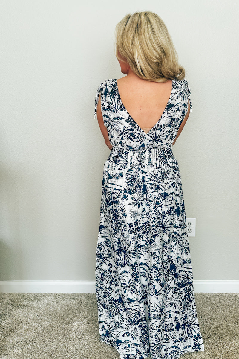 Back view of The Hawaiian Toile Maxi Dress featuring a deep V-neck back, smocked waist, and black and white tropical floral print.