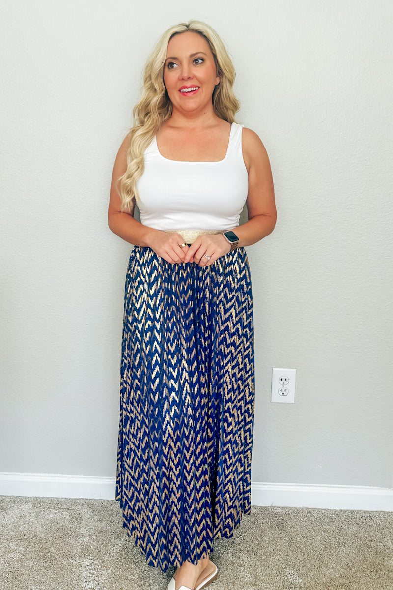 Blonde woman smiling in a white scoop neck tank top and the Monaco Metallic Pleated Skirt, a blue and gold chevron maxi skirt from an online Southern boutique.