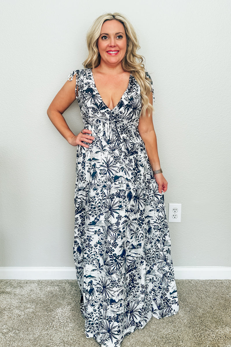 Front full-length view of blonde woman wearing The Hawaiian Toile Maxi Dress with a smocked waist, deep V-neckline, and tie straps.